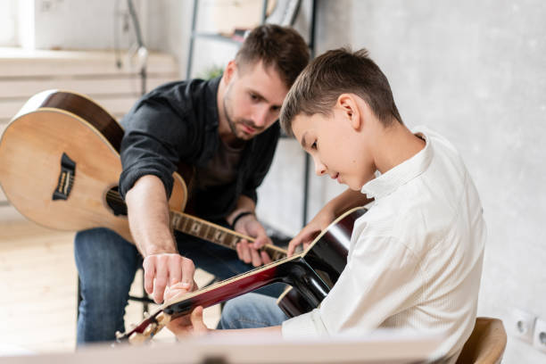 Adult man explains his son, who learn to play guitar, how to play studied chord correctly. Education with family Adult man explains his son, who learn to play guitar, how to play studied chord correctly. Education with family. father and son guitar stock pictures, royalty-free photos & images