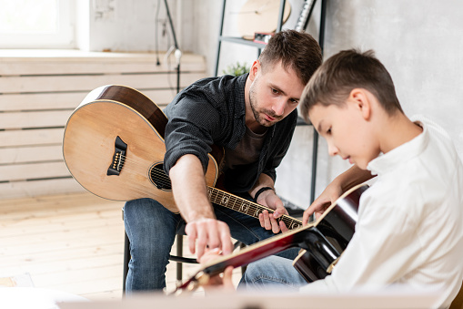 Two brother playing guitar. Older brother teaches younger one to play chords correctly.