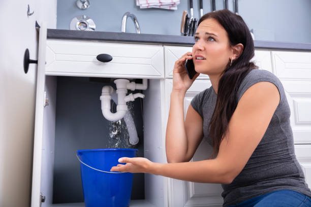 istock Woman Calling Plumber While Collecting Water Leaking From Sink 1166079474
