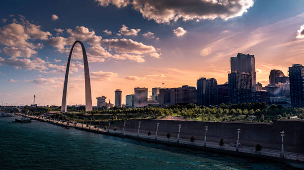 Mississippi river flowing infront of St Louis riverfront and downtown skyline and the Jefferson Expansion Memorial during summer. saint louis, MO--July 27, 2019; sunsetting behind gateway arch national park and midwestern skyscrapers on a cloudy summer day jefferson national expansion memorial park stock pictures, royalty-free photos & images