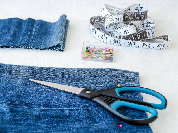 istock Making shorts out of blue jeans with multi colored headed sewing pins, white tailor tape with centimeters and inches and scissors. Shorten the jeans. DIY shorts out of jeans. 1166084652
