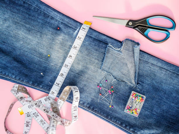 Blue jeans with large hole folded in half, sewing pins in a box, white tailor tape with centimeters and inches and scissors. Shorten the jeans. DIY shorts out of jeans. stock photo