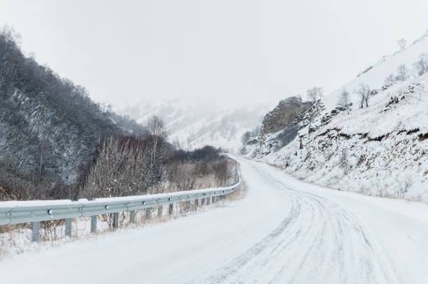 istock Empty mountain asphalt road in winter covered with snow on a cloudy day. 1166089702