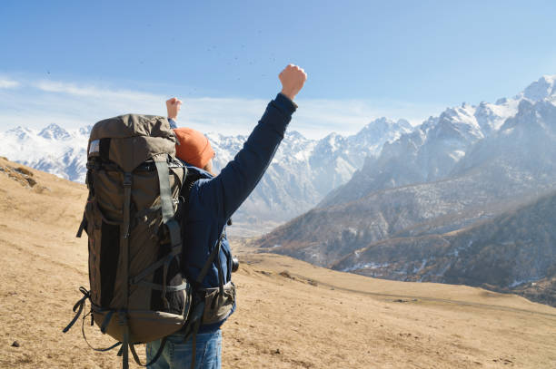 istock A bearded man in a hat and a backpack is standing outdoors against the snowy mountain peaks on a sunny day. 1166090828