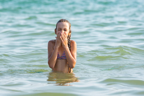 The girl drowned in sea water and wipes her nose and face with her hands stock photo