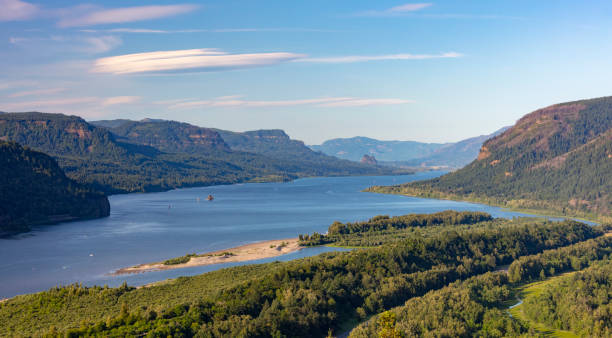 View across the Columbia River Valley, a lush landscape filled with dense pine forests and rocky mountain ridges.Taken at Beacon Rock State Park, a public recreation area and a massive basalt rock column in the Columbia River Gorge.