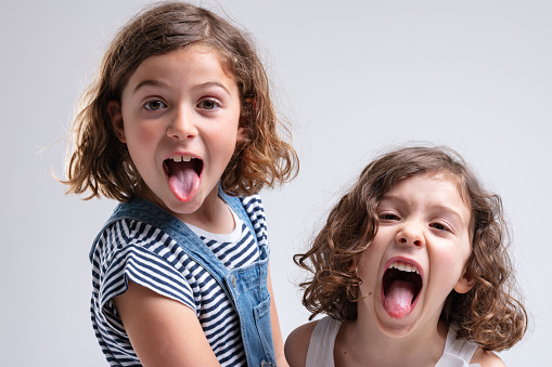 Playful little girls sticking out their tongues at the camera as they stand stand by side on a white background