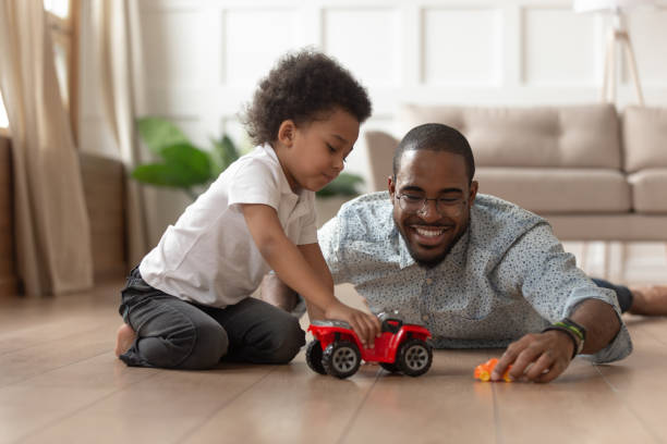 papà nero sorridente che gioca alle auto giocattolo con il figlio piccolo - child exercising little boys toddler foto e immagini stock