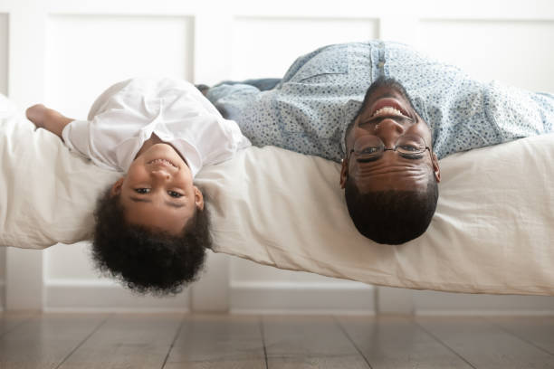 uśmiechnięty czarny tata i syn malucha leżący do góry nogami - male men black african descent zdjęcia i obrazy z banku zdjęć