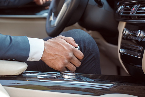 Young businessman driver sitting inside the car holding gear shifter close-up