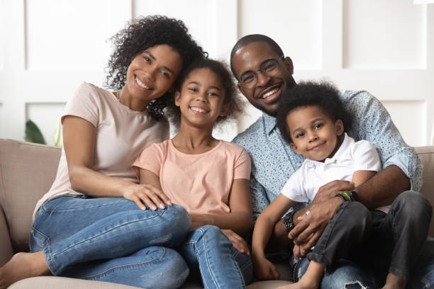 Portrait of black family with kids relax on couch Portrait of happy young african American family with little kids sit relax on couch cuddling, smiling black parents rest on sofa hug preschooler children posing for picture at home together family with two children stock pictures, royalty-free photos & images