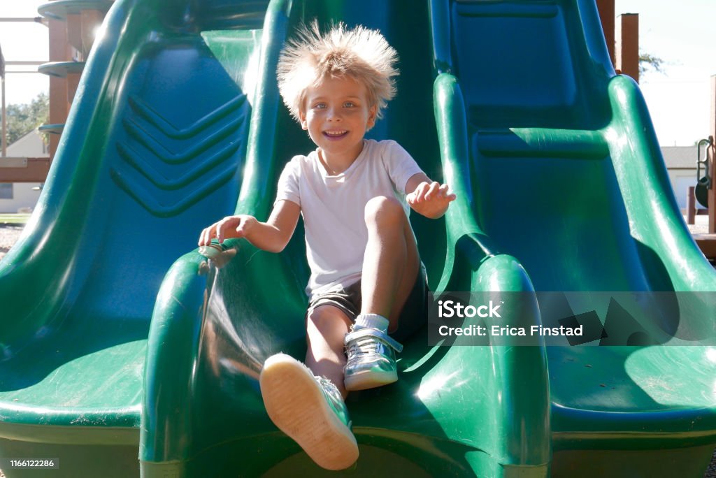 Smiling boy on slide with hair sticking up Cute, young boy smiling as he goes down a green slide. Static electricity is making his blonde hair stick up. Static Electricity Stock Photo
