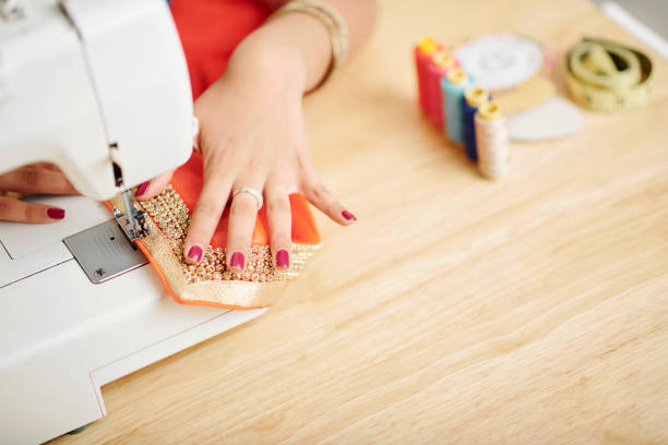 Close-up image of woman working on sewing machine and making sari with beautiful golden embroidery