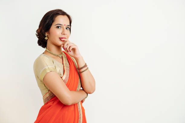 Portrait of young pensive Indian woman in national dress biting her finger and looking at camera, isolated on white