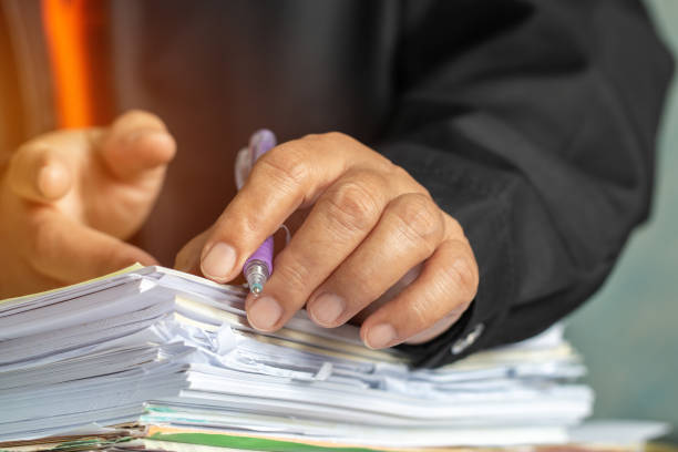 mãos do homem de negócios que verific documentos arquivo mercado financeiro, pesquisando a informação no escritório ocupado da mesa do trabalho. as pilhas do original inacabado conseguem com a pena para o suspiro. conceito do relatório do negócio - legal system document report examining - fotografias e filmes do acervo