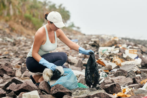 o voluntário da mulher nas luvas prende o lixo plástico no fundo da costa de mar. - mulher catando lixo - fotografias e filmes do acervo