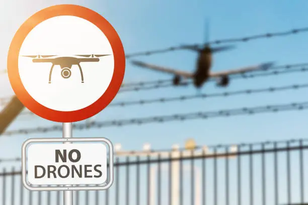 close-up of drone prohobition sign against security fence and airplane landing on airport