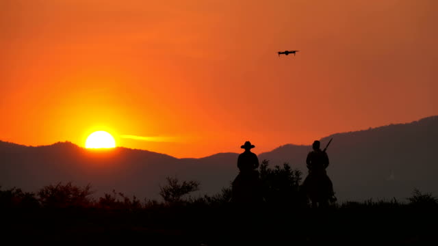 Drone Camera Flying To Shooting Shot Of Soldier And Cowboy Riding Horses Walking Into The Sunset