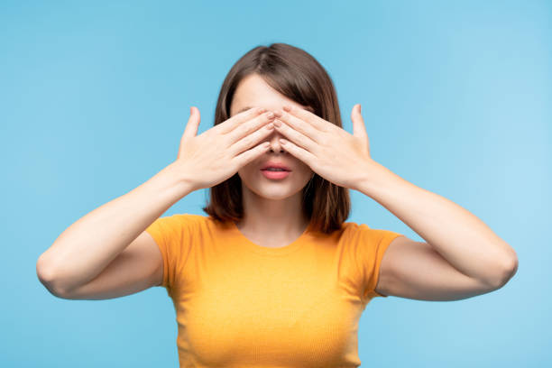 joven morena hembra en camiseta amarilla cubriendo sus ojos con las manos - venda de ojos fotografías e imágenes de stock