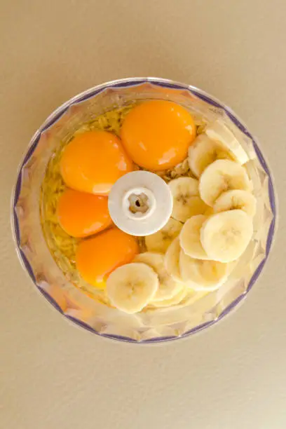 Blender bowl with eggs and banana slices with cereals on wooden cutting board , eating healthy concept