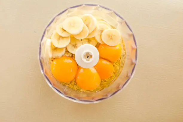Blender bowl with eggs and banana slices with cereals on wooden cutting board , eating healthy concept