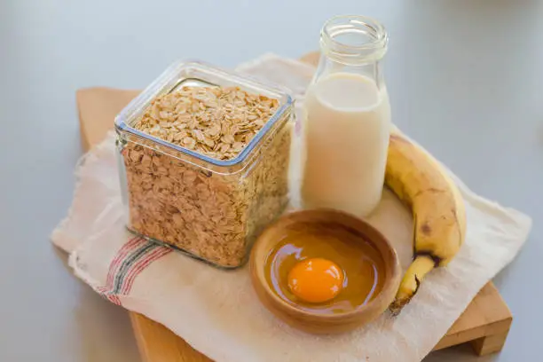 Bowl with egg and banana with cereals in glass jar with milk bottle on table, ingredients for cocking pancakes concept