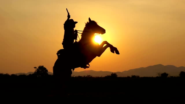 Slow Motion Shot Of Cowboy Riding Horse And Holding A Gun At Sunset