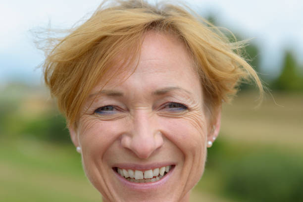 Happy woman with a warm friendly smile and neat short red blond hair in a close up head portrait outdoors