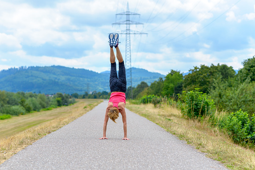 Agile woman doing a handstand on a quiet rural road with mountain backdrop in a concept of suppleness, health and an active lifestyle