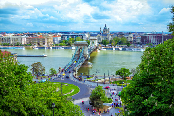Spring cityscape of Budapest with Danube River, Chain bridge and Adam Clark Square Budapest/Hungary- April 30, 2019: spring cityscape with Danube River, Chain bridge, road and traffic, Adam Clark Square with green trees and lawns, beautiful historic architecture budapest danube river cruise hungary stock pictures, royalty-free photos & images