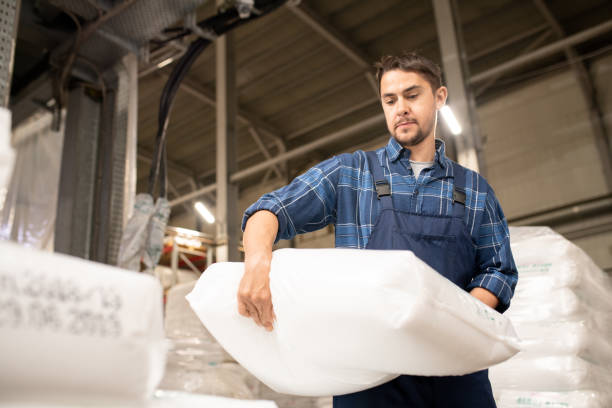 istock Young man in workwear carrying heavy white sack with polymer granules 1166164567