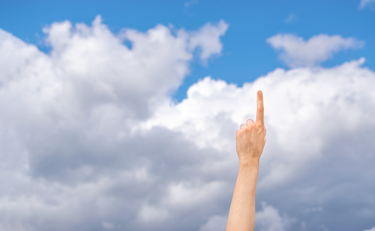 Female raised hand pointing finger in the air with sky and clouds on background. Idea concept. Copy space.