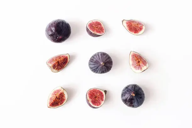 Photo of Fresh ripened purple figs. Creative square composition of the whole and sliced exotic fruit and isolated on white table background. Decorative pattern. Flat lay, top view from above. Food photography.