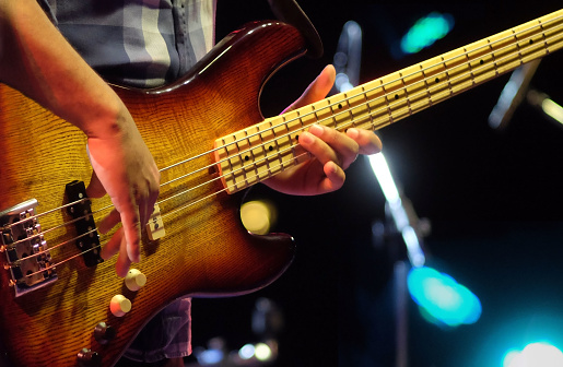 Professional musician plays electrical bass guitar solo on concert stage. Sring musical instrument on jazz concert.