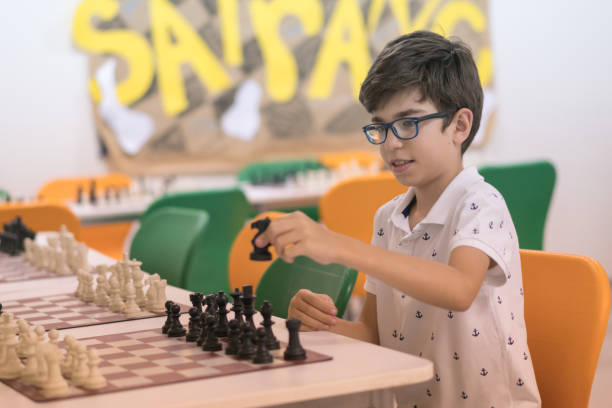 glücklicher junge im klassenzimmer spielt schach - concentration chess playing playful stock-fotos und bilder