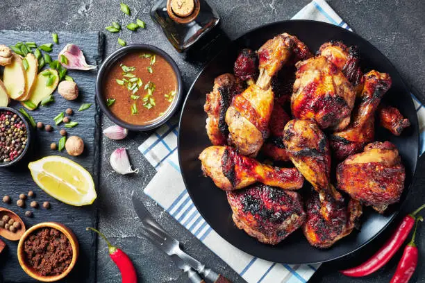 Spicy Grilled Caribbean Jerk Chicken drumsticks and thighs on a black platter on a wooden table