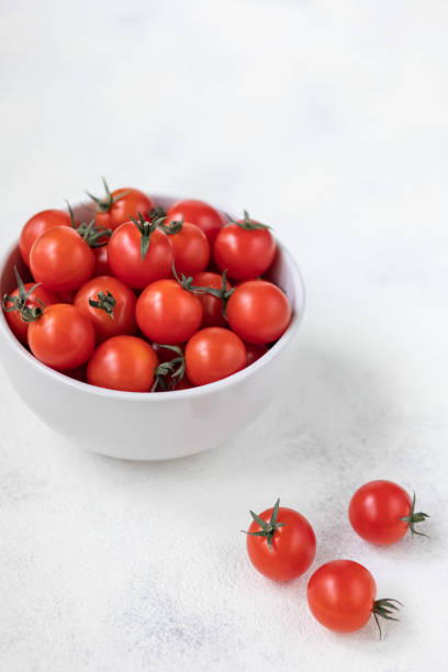 istock Cherry tomatoes in a bowl and on a white textural background, top view, vertical shot 1166172589