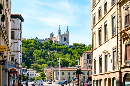 The Basilica Notre Dame De Fourviere seen up on the hill in Lyon, France, a warm day in the summer. In front residential buildings and shops along the street.