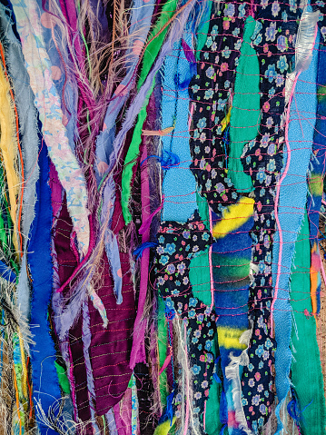Colourful torn fabric strips, cords and wool, sewn together in a striped pattern. Textile art textured background. Vertical.