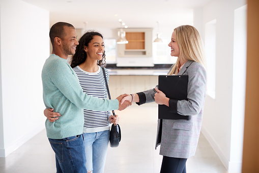 Female Real Estate Agent Shaking Hands With Couple Interested In Buying House