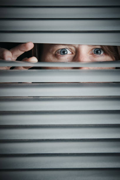 istock Young woman peeps suspiciously through venetian blind 1166188604
