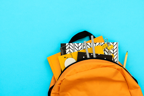 Back to school concept. Backpack with school supplies on blue background. Top view. Copy space. Flat lay