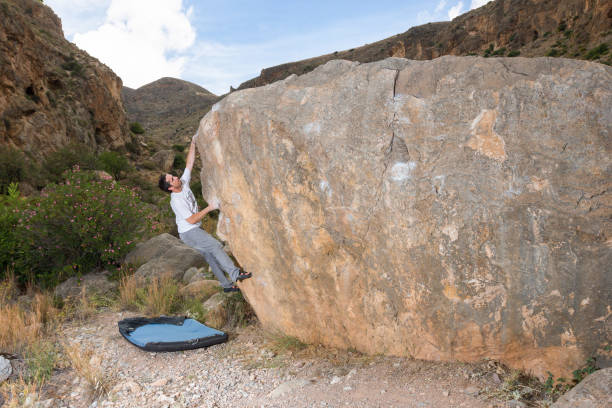 istock Climber ascending a boulder with his crash-pad protecting him 1166190118