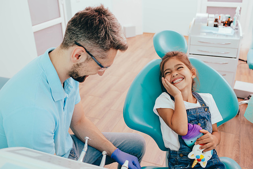 Little girl laughing while sitting in dentists chair . Little patient after successful teeth treatment. Pediatric dentistry