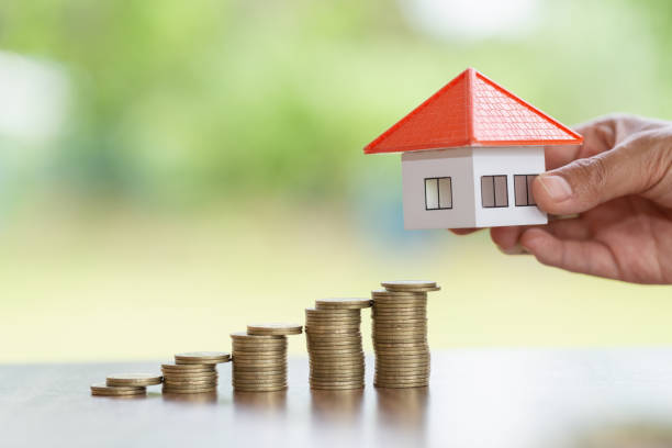 istock Woman's hand putting house model on coins stack. Concept for property ladder, planning savings money of coins to buy a home concept property mortgage and investment for a house. 1166192151