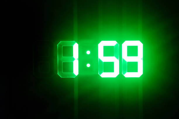 istock Green glowing digital clocks in the dark show 1:59 time 1166193124
