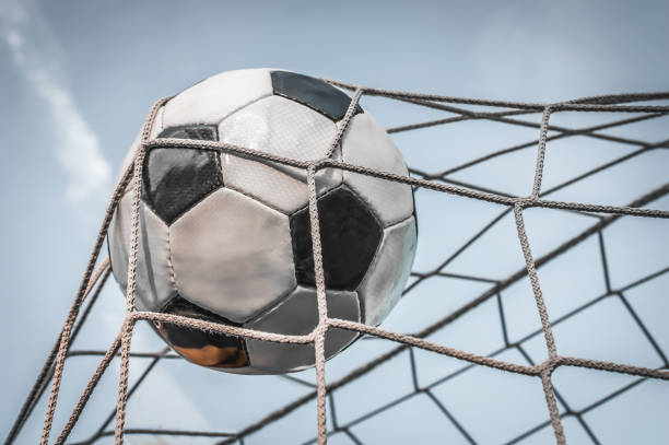 Soccer ball in the goal net with blue sky background and sunset