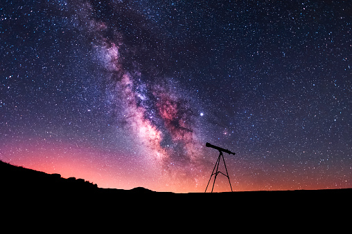 Silhouette of a telescope at the starry night and bright milky way galaxy.