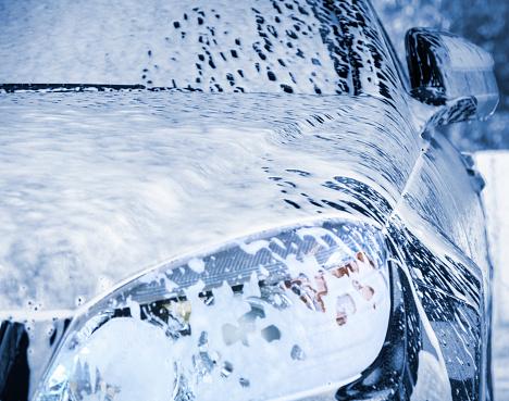 Hamburg, Germany - August 2. 2019:  Front view of the right fender for A blue mercedes car in the open car wash. The vehicle is foamed in the pre-wash cycle. The vehicle is completely foamed. No people in this image.