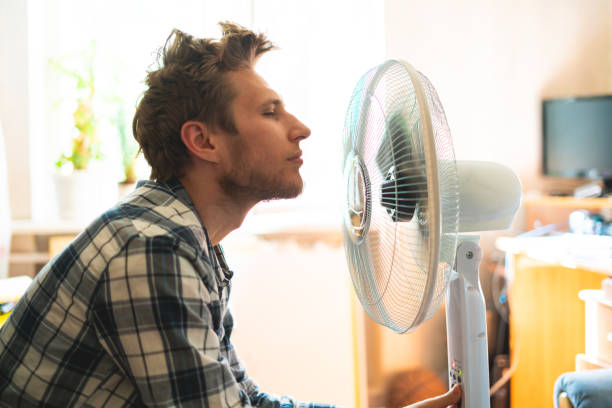 person, die den elektrischen ventilator genießt, sein gesicht zu hause kühlt, während der sommerhitze - summer cool electric fan heat stock-fotos und bilder